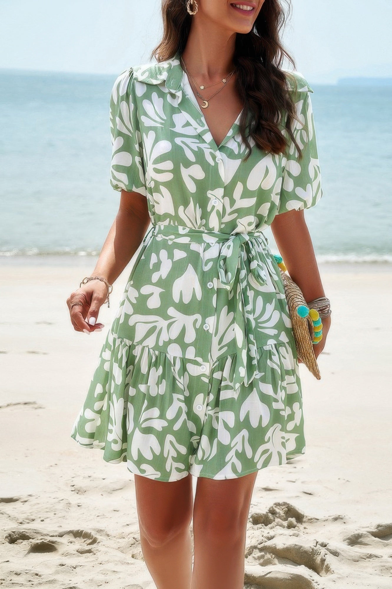 Model on beach in leaf print button down mini dress by SplendorAmoris, with belted ruffle and accessories for tropical casual vibe